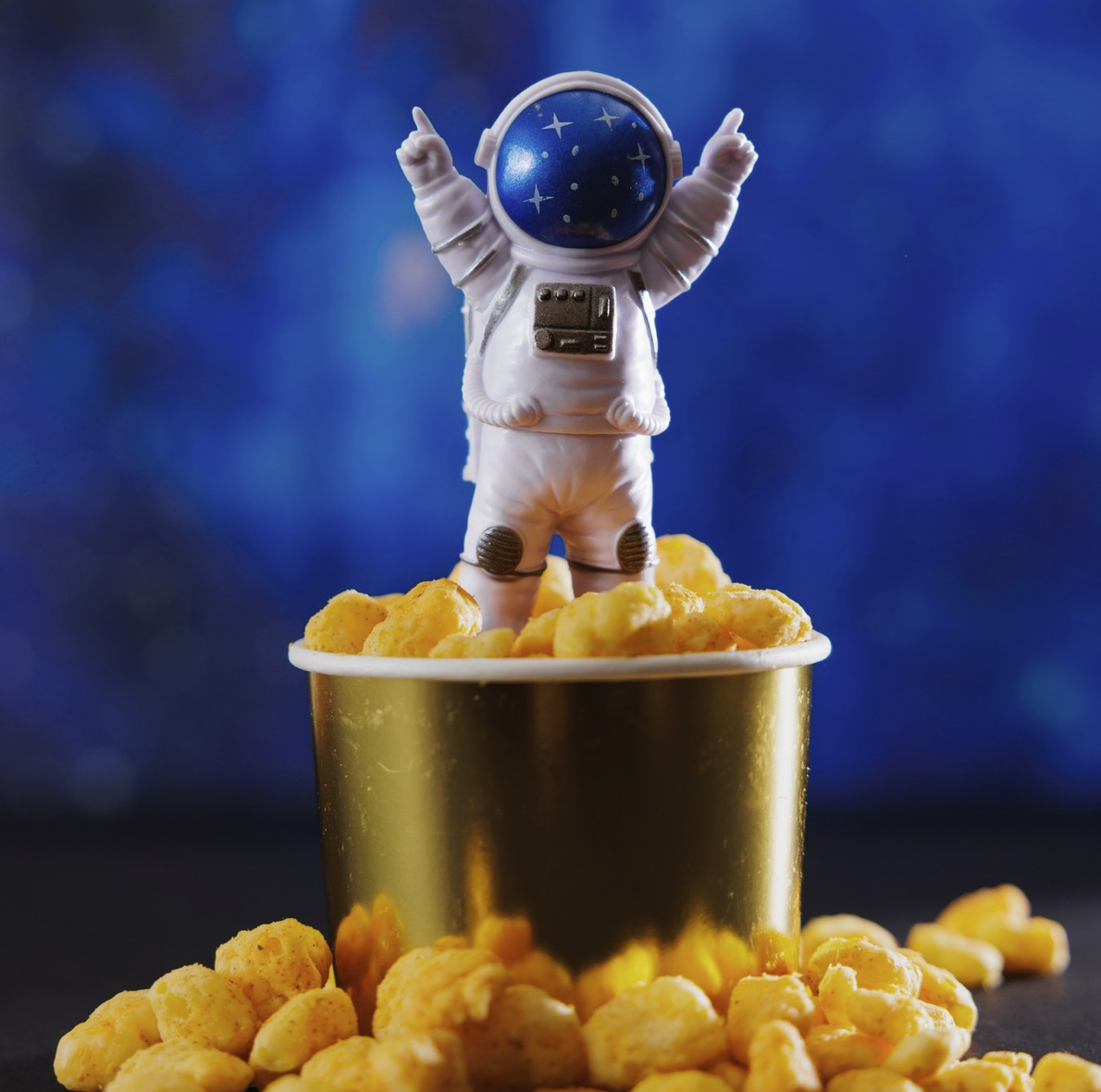 Playful astronaut figure standing in bucket of Moon Cheese bites against blue space background